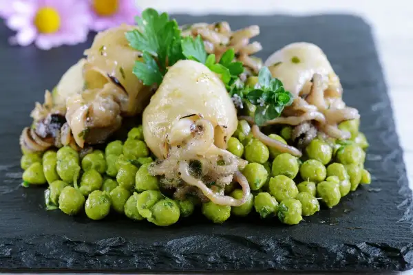Delizioso piatto di seppie con piselli, guarnito con prezzemolo e erbe aromatiche, servito su una pietra scura.