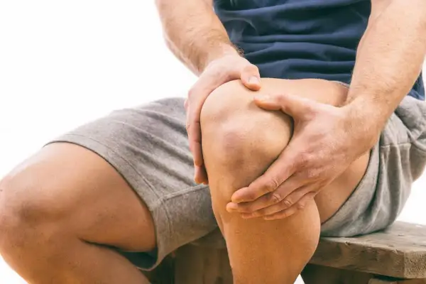 Uomo con dolore al ginocchio, mani che stringono l'articolazione. Possibile problema al menisco, consulta un osteopata.