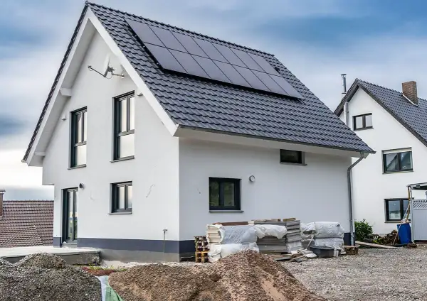 Nowy dom z panelami słonecznymi na dachu, w trakcie rozbudowy. Wokół materiały budowlane.