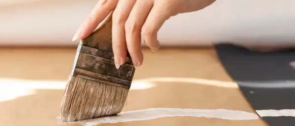 Main d'une personne peignant une surface en MDF avec un pinceau blanc.