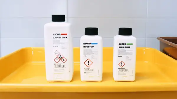 Three Ilford bottles for developing, stopping, and fixing film sit in a yellow tray, ready for creating the best black and white film.