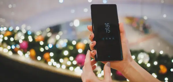 Ręce trzymające czarny smartfon Samsung, na ekranie zegar i ikony. Planowane zgranie kontaktów z Samsunga na komputer.