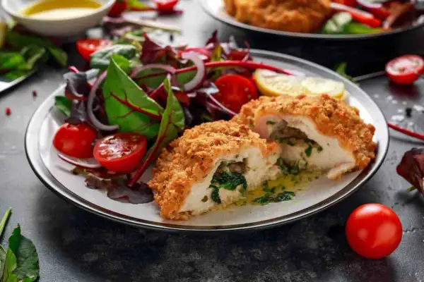Pollo alla Kiev croccante, ripieno di spinaci e burro, servito con un'insalata fresca di pomodorini e cipolla rossa.
