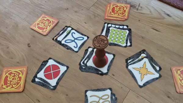Karty gry Jungle Speed rozłożone na podłodze, gotowe do szybkiej rozgrywki. Drewniany totem pośrodku.