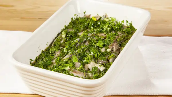 Acciughe al verde in una teglia bianca, condite con abbondante prezzemolo tritato e aglio.
