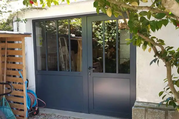 Remplacer porte de garage par fenêtre : une nouvelle entrée lumineuse avec des portes vitrées grises. Des outils de jardin sont rangés à gauche.