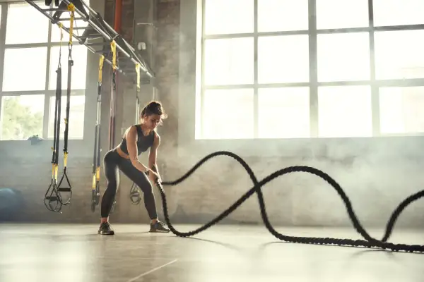 Kobieta ćwiczy z linami treningowymi, pokazując, crossfit co to jest – intensywny trening całego ciała.