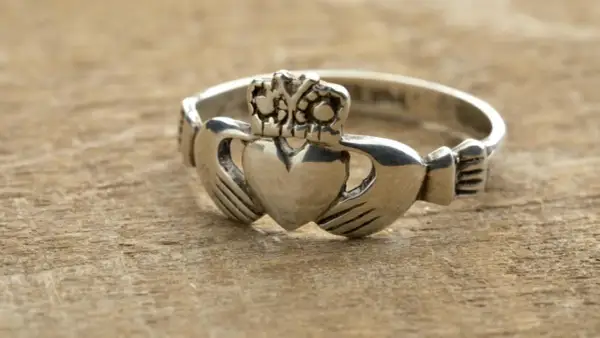 Anillo Claddagh de color oro blanco, con corazón, manos y corona, sobre madera.