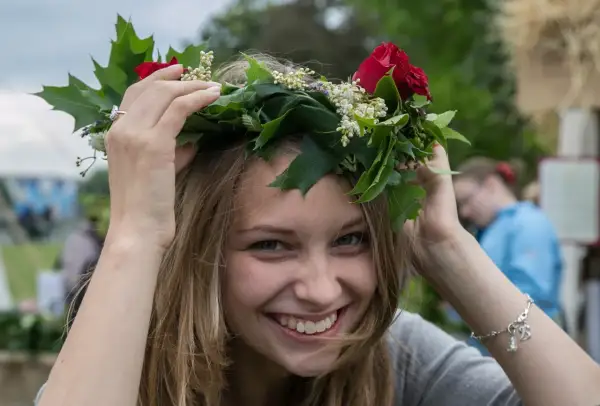 Uśmiechnięta dziewczyna w wianku z czerwonych róż i zielonych liści, jak na krakowskim festynie.