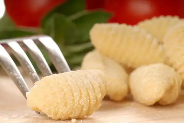 Une fourchette pique un gnocchi fait maison, prêt pour une délicieuse recette gnocchi. Des gnocchis frais et des ingrédients italiens en arrière-plan.