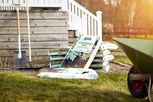 Säckar med planteringsjord, en spade och en kratta står redo för trädgårdsarbetet. Den kalkrika jorden är perfekt för att ge dina växter en bra start.