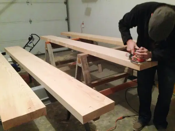 Man sanding Douglas fir planks on sawhorses, preparing them for staining.