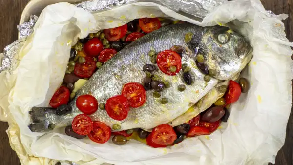 Orata al cartoccio con pomodorini, olive e capperi, cotta in forno.