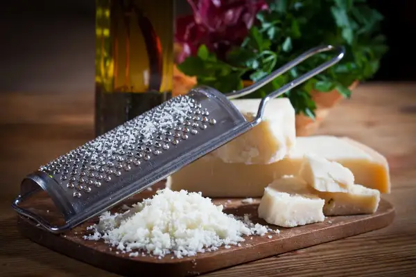 Tarka z grudkami sera, obok kawałki sera Grana Padano i parmezan. W tle butelka oliwy i zielenina.