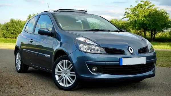 Un Renault Clio azul aparcado en un camino rural. El coche tiene un techo solar y llantas plateadas.