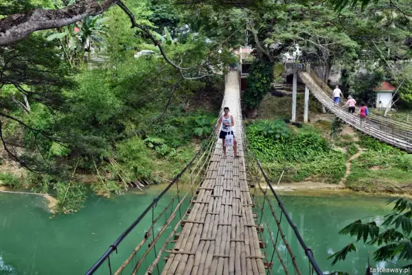Młody mężczyzna idzie przez bambusowy most wiszący nad turkusową rzeką na Bohol, Filipiny.