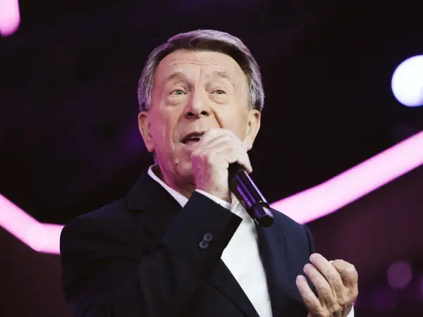 Wojciech Gąssowski śpiewa "Gdzie się podziały tamte prywatki". Artysta w czarnym garniturze i białej koszuli, z mikrofonem w dłoni, na tle fioletowych świateł.