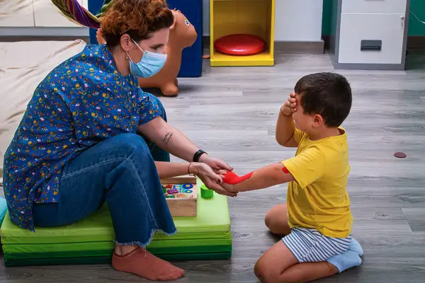 Niña recibe terapia ocupacional infantil, con un terapeuta aplicando pintura roja en su brazo.