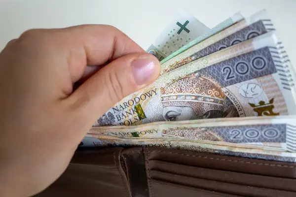 Dłoń wkłada polskie banknoty 200 zł do portfela. Zastanawiasz się, ile wynosi składka zdrowotna?