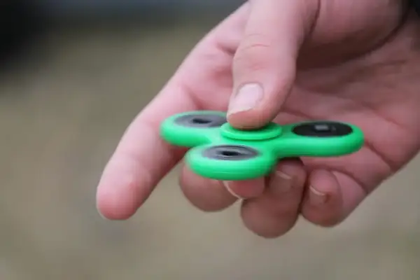 Groene fidget spinner in hand, een hulpmiddel voor concentratie bij hoog functionerend autisme.