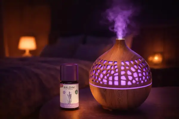 Ein Diffusor verströmt lila Dampf, daneben eine Flasche Baldini Lavendelöl. Perfekt für Lavendel Entspannung im Schlafzimmer.