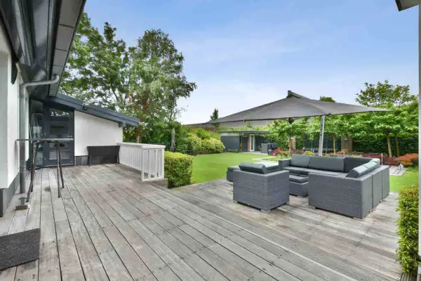 Aménagement coin détente extérieur avec salon de jardin gris sous un grand parasol, sur une terrasse en bois.