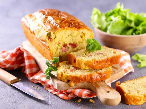 Un cake chorizo poivron, doré et moelleux, coupé en tranches sur une planche en bois. Une salade verte est servie à côté.