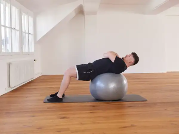 Un homme effectue un exercice avec ballon, le dos courbé sur le ballon de gym, les mains croisées sur la poitrine.
