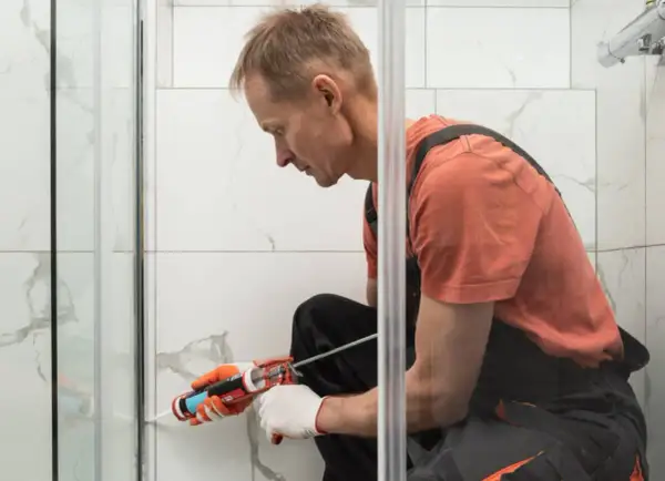 Hombre con guantes aplica sellador para plato de ducha.