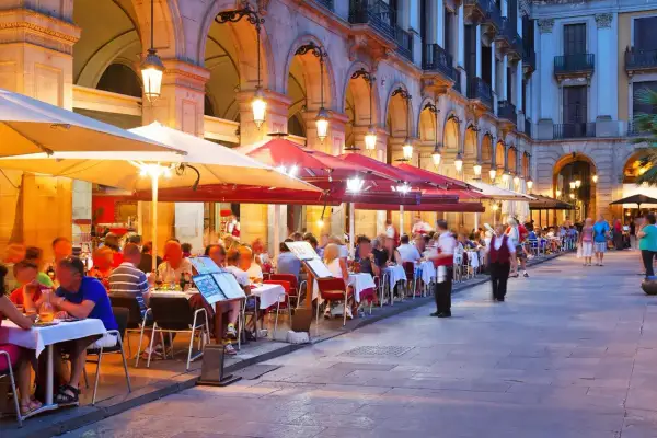 Kvällssol över många uteserveringar med folk som äter och dricker. En livlig atmosfär på restauranger i Barcelona.