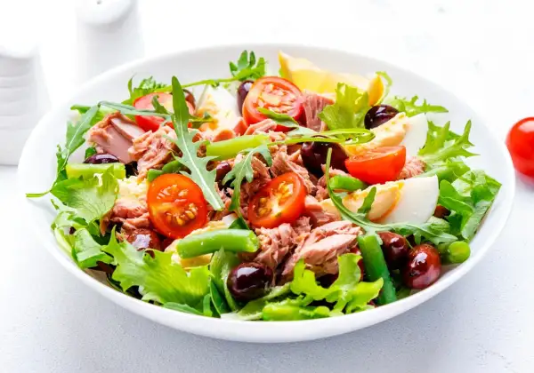 En fräsch sallad nicoise med tonfisk, ägg, tomater, oliver och gröna bönor på en bädd av sallad.