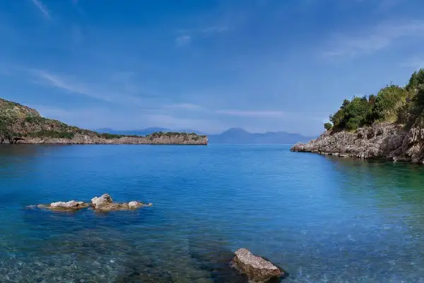 Calmo mare a maggio, con scogli affioranti e coste verdi sotto un cielo azzurro.