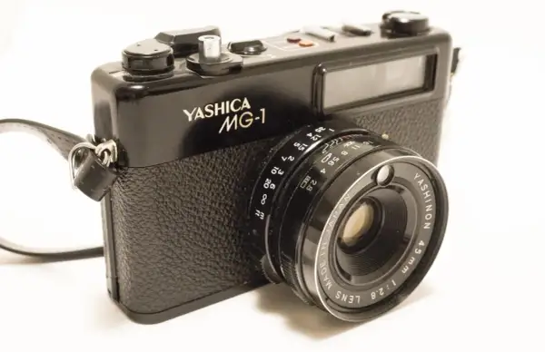 A black Yashica MG-1 camera with a leather strap. The lens reads "YASHINON 45mm 1:2.8".