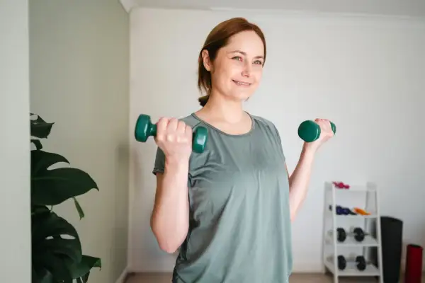 Lächelnde Frau macht Krafttraining mit Hanteln. Sie ist auf dem Weg zum Abnehmen und fühlt sich gut.