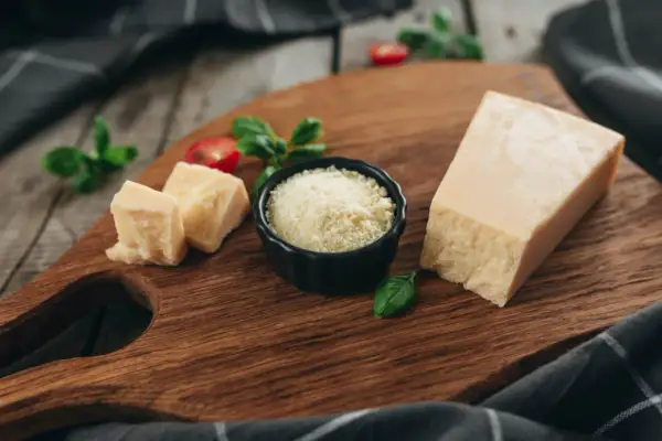 Kawałek parmezanu, pokrojony ser i starty ser do carbonary na drewnianej desce, ozdobione bazylią i pomidorkami.