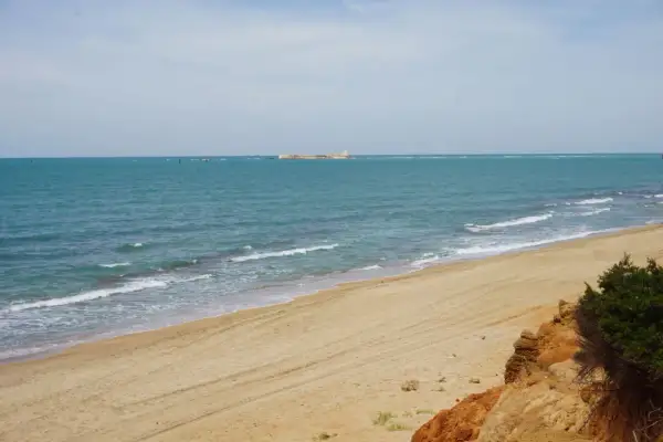 Playa de arena dorada con mar turquesa y una estructura en el horizonte. Un rincón idílico de las calas Chiclana.