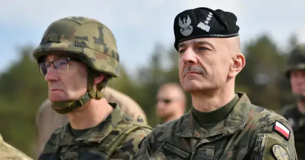 Generał Andrzejczak w czapce z orłem i gwiazdkami, obok żołnierz w hełmie.
