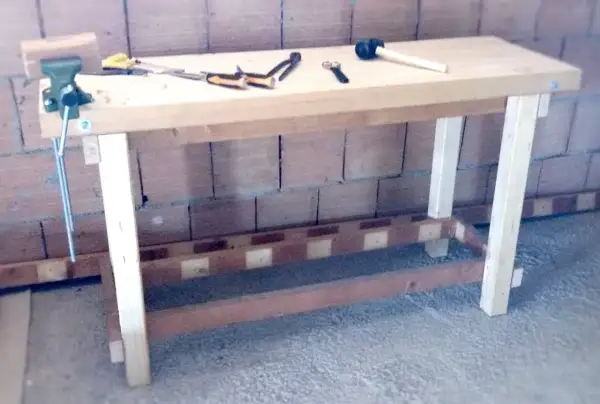 Un banco da lavoro in legno, pronto per iniziare a fare un tavolo in legno. Attrezzi come morsa, martello e pinze sono pronti all'uso.