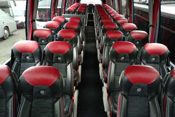 Wnętrze autobusu z rzędami czerwono-czarnych siedzeń. Zastanawiasz się, ile może jechać kierowca, gdy wszyscy pasażerowie są już na swoich miejscach.