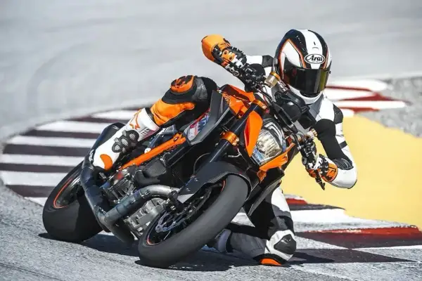 Motocyklista w kombinezonie pochyla się na torze wyścigowym na pomarańczowym motocyklu KTM Super Duke.