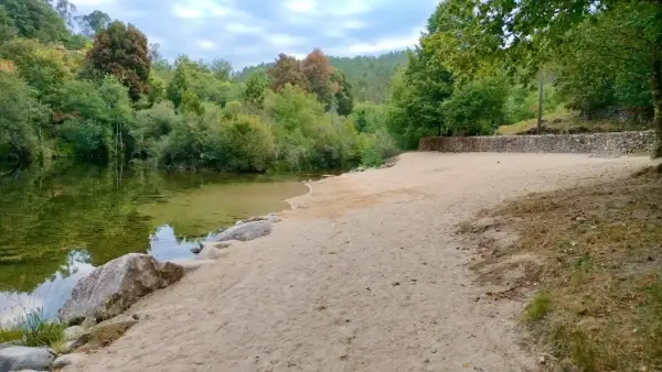 Tranquila playa fluvial en Fornelos de Montes, con arena dorada, aguas cristalinas y rodeada de exuberante vegetación.