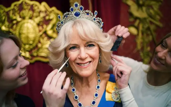 Camilla, drottningen, får smink och hår fixat. Hon bär en tiara och ett blått halsband.