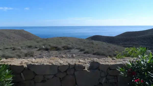Vista desde una mesa roldan, con el mar azul al fondo y colinas áridas cubiertas de vegetación baja.