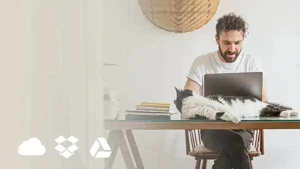 Mężczyzna pracuje przy laptopie, a kot leży na biurku. Ikony chmury, pudełka i trójkąta symbolizują online photo storage options.