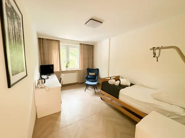 Pokój hotelowy z łóżkiem, biurkiem, fotelem i obrazem z lasem.