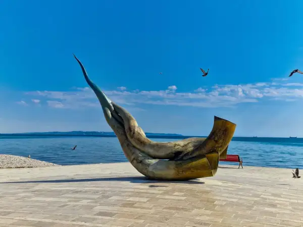 Monumentalna rzeźba na promenadzie w Durrës, plaża w tle, błękitne niebo i morze.