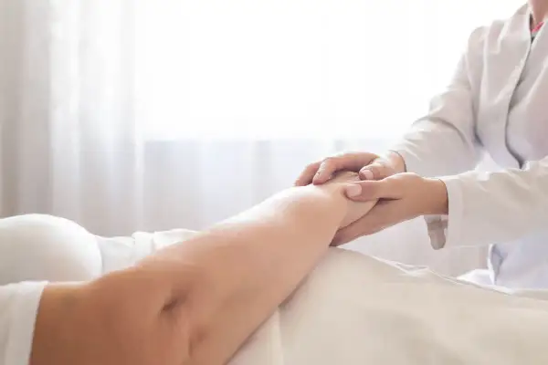 Delikatne dotknięcie dłoni pielęgniarki na ramieniu pacjenta, wskazujące na troskę i pomoc w procesie, jak wyleczyć odleżyny.