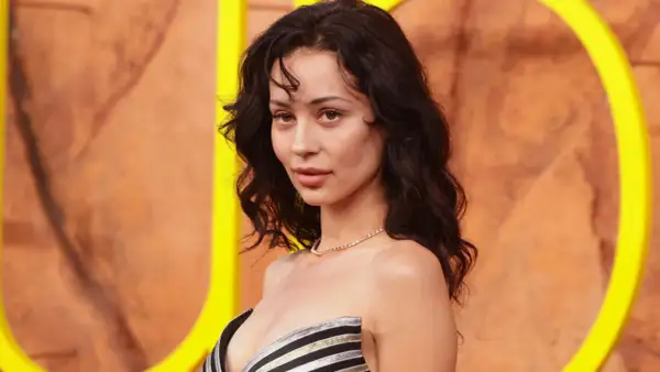 Alexa Demie, con cabello oscuro y ondulado, luce un collar de diamantes y un vestido a rayas.
