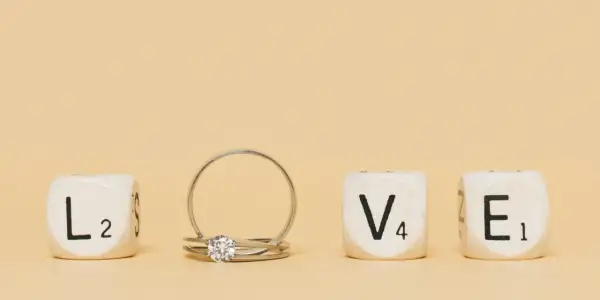 Un anillo inicial de oro con un diamante, junto a cubos que forman la palabra "LOVE".