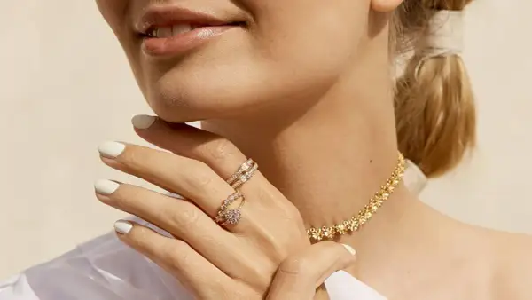 Manos con manicura blanca luciendo dos anillos de **joyería Suárez anillos** y un collar dorado.